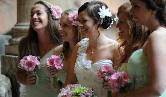 A bride with a chic updo adorned with floral accents, surrounded by her bridesmaids holding pink bouquets, showcasing Jyn San Hair & Makeup's bridal and bridal party styling services in Somerset.