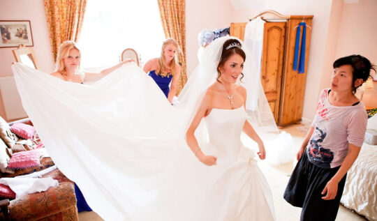 A radiant bride with an elegant tiara and flawless makeup, supported by her bridal party and stylist Jyn San, showcasing expert hair and makeup preparation for a perfect wedding day in Somerset