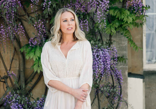 Her hair is styled in soft waves, and her natural makeup highlights her glowing complexion